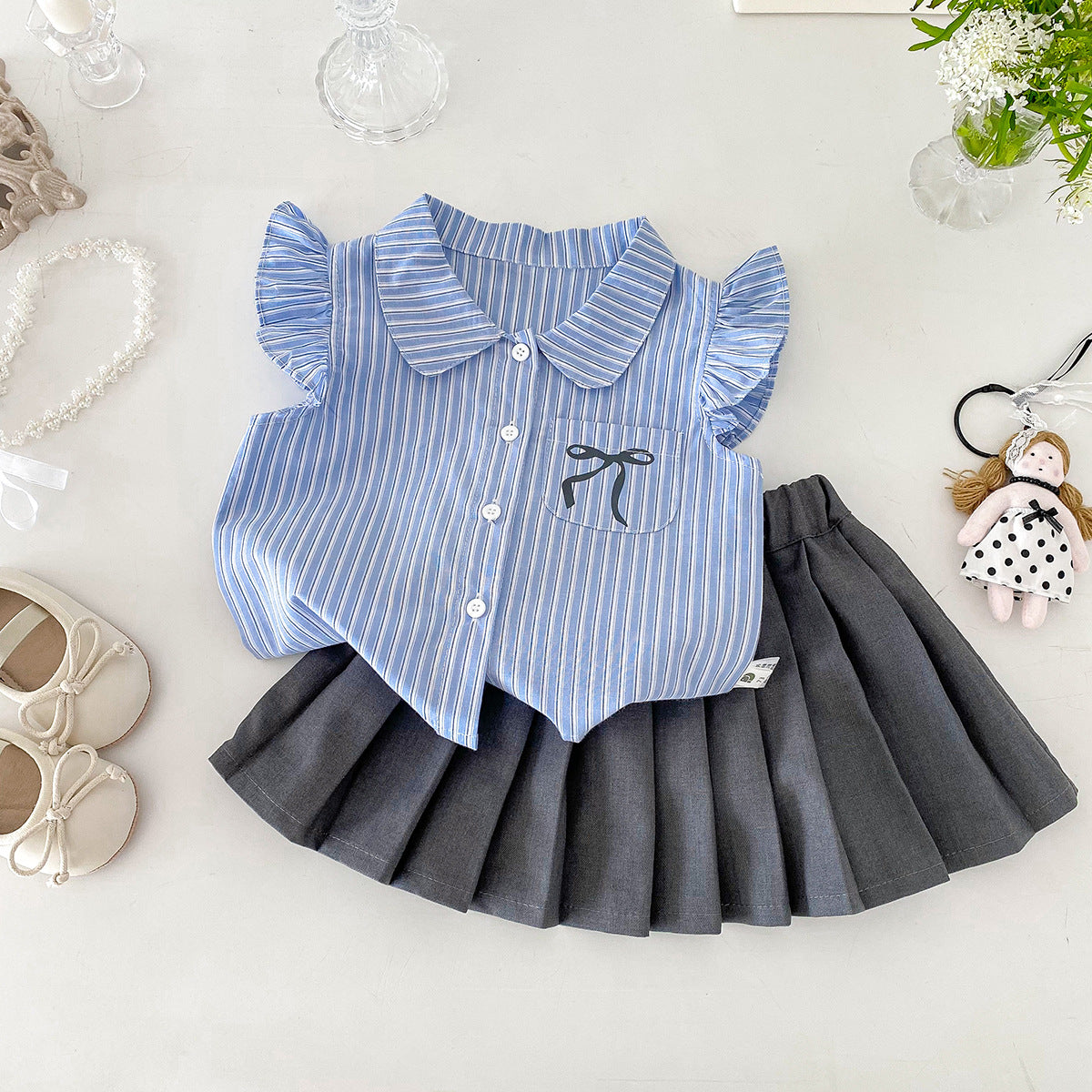 A set of a flutter-sleeved shirt and a pleated skirt in the collegiate style for little girls in summer