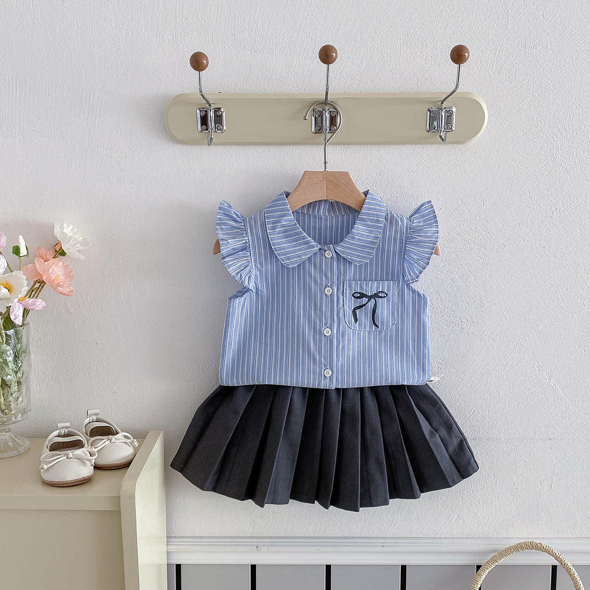 A set of a flutter-sleeved shirt and a pleated skirt in the collegiate style for little girls in summer
