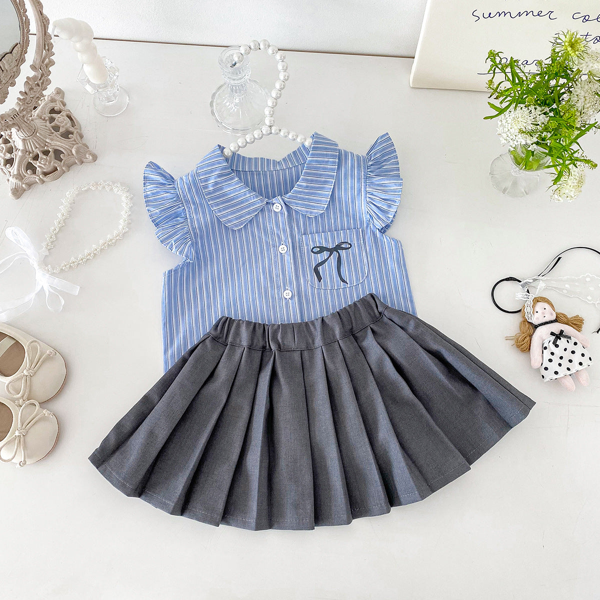 A set of a flutter-sleeved shirt and a pleated skirt in the collegiate style for little girls in summer