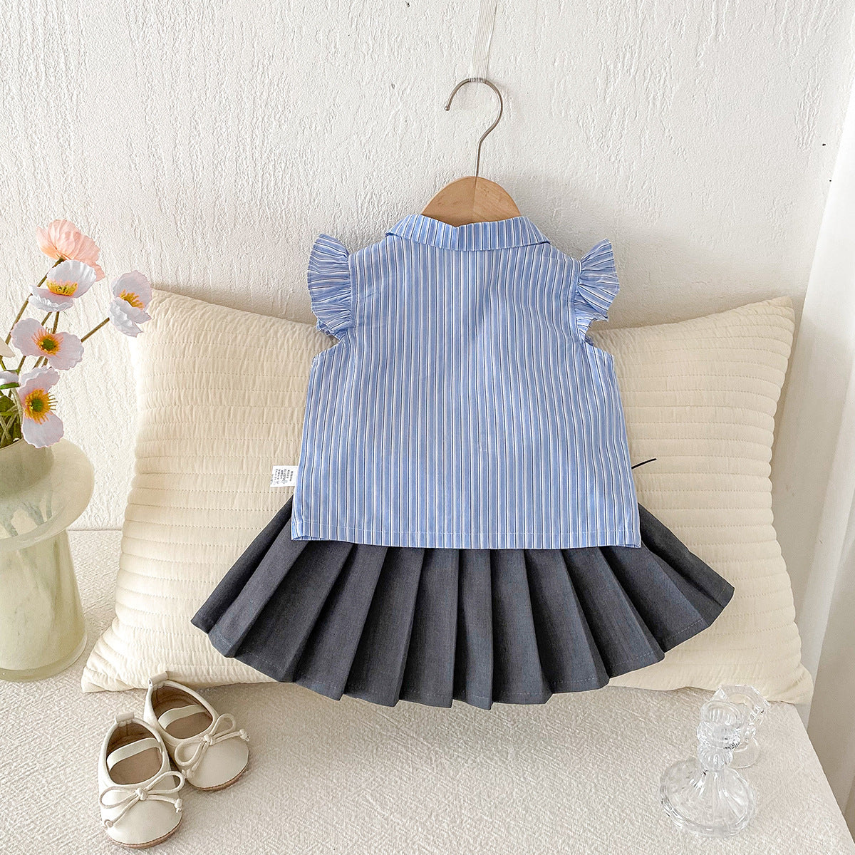 A set of a flutter-sleeved shirt and a pleated skirt in the collegiate style for little girls in summer